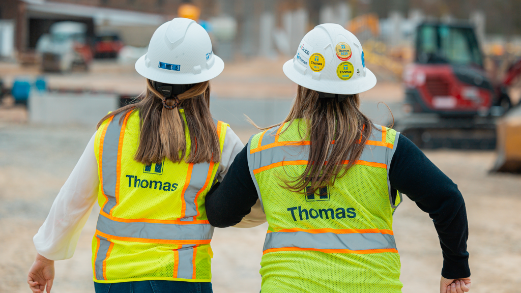 Two female Thomas employees walking on a jobsite with arms linked